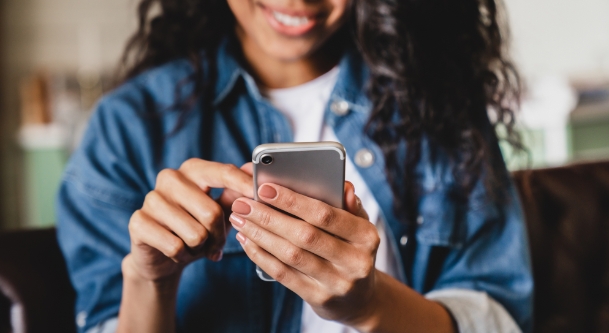 Woman in Jean jacket smiling while looking at her phone