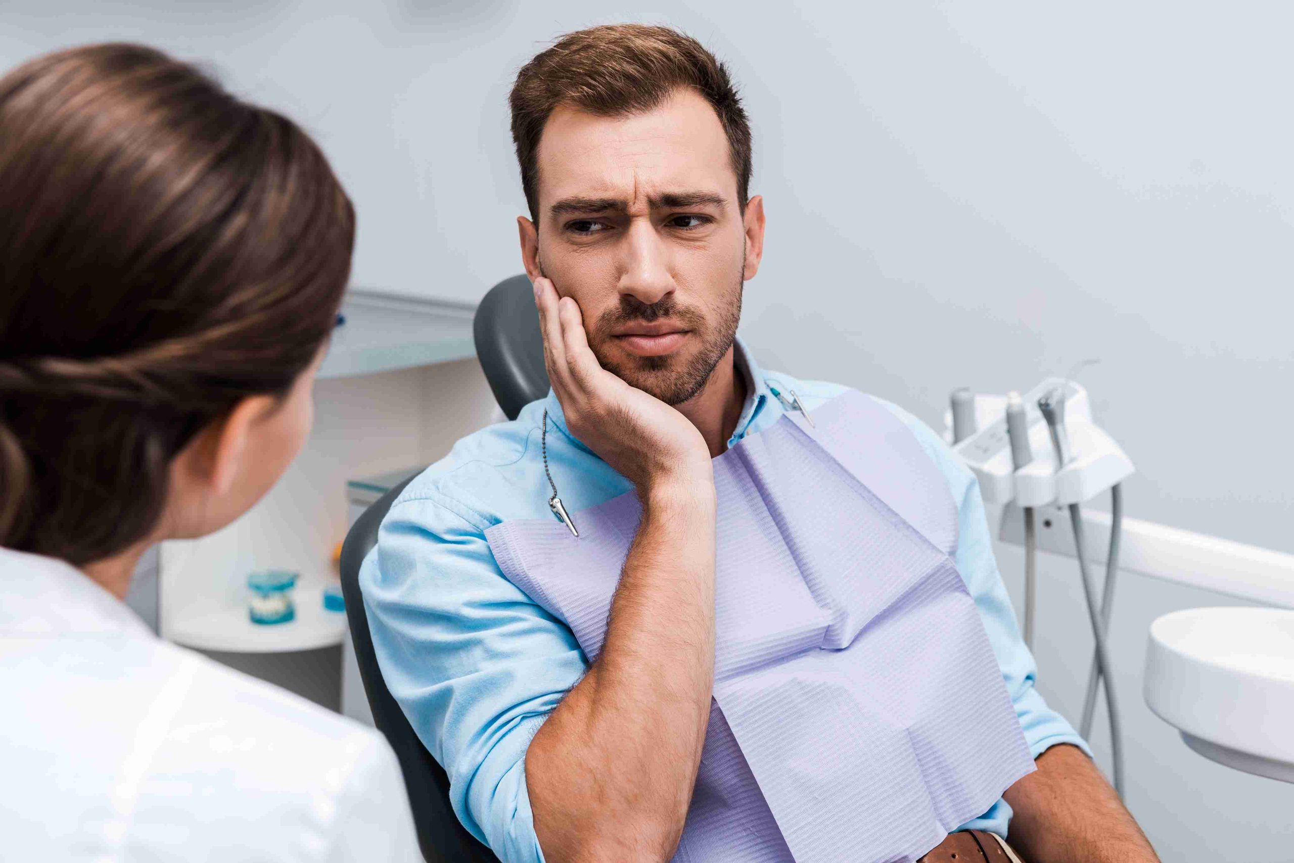 Patient experiencing tooth pain while speaking with a dentist.